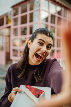 Laughing woman taking a selfie with cheesecake