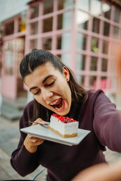 Woman enjoying strawberry cheesecake at an outdoor cafe