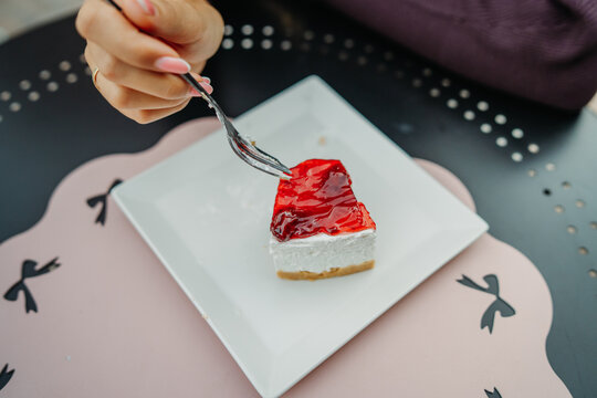 Hand reaching for a slice of strawberry cheesecake with a fork