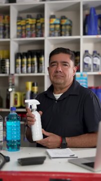 Hispanic auto mechanic presenting cleaning spray bottle while talking in the auto shop