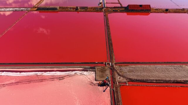 Red water in salt evaporation basins. Aerial shot of intense red water in salt evaporation basins, separated by narrow earthen dikes with train tracks.