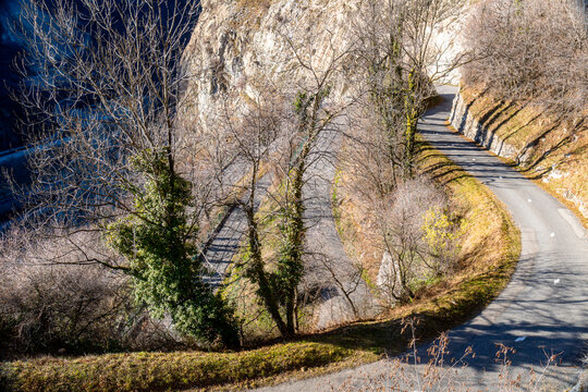 View of the famous Lacets de Montvernier switchback road winding up a steep mountainside with bare trees and rocky slopes in Montvernier, Auvergne-Rhone-Alpes, France.