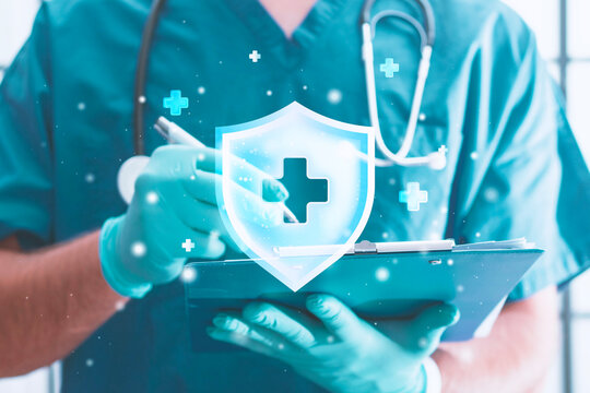 Doctor in surgical scrubs writing on clipboard with glowing medical cross shield icon double exposure. Health insurance, healthcare security, patient protection and medical technology concept.