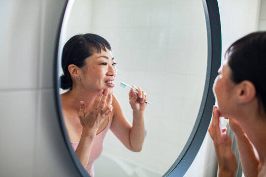Woman checking skin while brushing teeth in bathroom