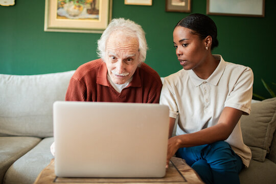 Young woman helping senior man on laptop at home