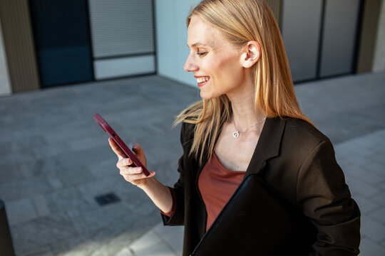 Smiling businesswoman checking smartphone outside office building