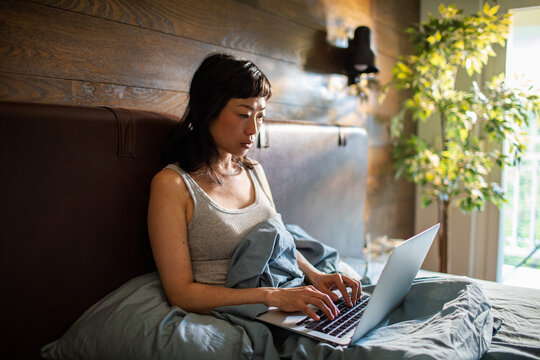 Woman typing on laptop in bed at home