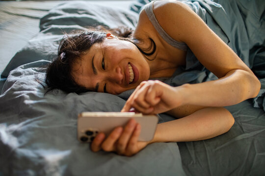 Smiling woman texting on smartphone in bed