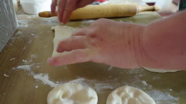 Hands shape dumplings on floured board. Rolling pin rests nearby, ready for use. Flour dusts work surface, showing busy kitchen. Warm, homely scene captures cooking moment. Great for food, cultural