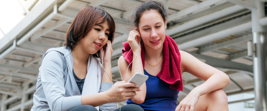 Banner Sport Fitness Two Woman listen to music together after exercise in modern city wear sportswear. Healthy wellness Two Young asian woman smile, laugh using headphone after workout exercise