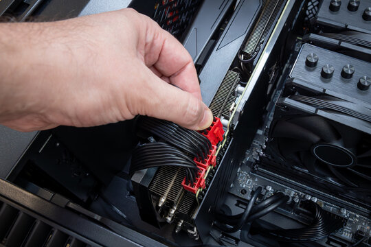 Close up of a hand connecting red modular PCI power connectors to a powerful graphics card inside a PC case. Building or upgrading a powerful gaming PC