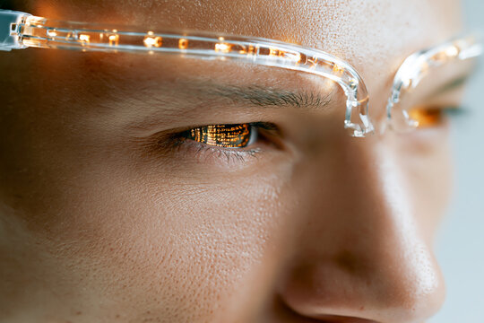 Close up of a mans eyes with digital data code reflection wearing smart glasses with glowing orange light guides. Futuristic technology concept of cyberware and human cyborg.