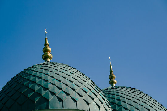 View of the intricate green tiled domes of the Minor Mosque topped with golden spires against a clear blue sky in Tashkent, Uzbekistan.