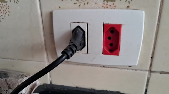 Black electrical plug inserted into white wall outlet socket interior