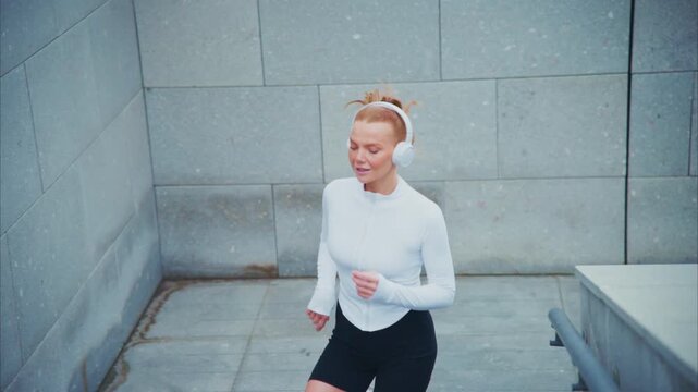Young woman runs with headphones on. Hair flies as she moves through city. She smiles, enjoying her workout. Footage captures active, happy lifestyle. Ideal for fitness, wellness
