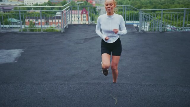 Athletic woman runs on rooftop path. Cityscape stretches behind her. She moves forward with focused determination. Urban fitness scene, active lifestyle. Ideal for health, wellness