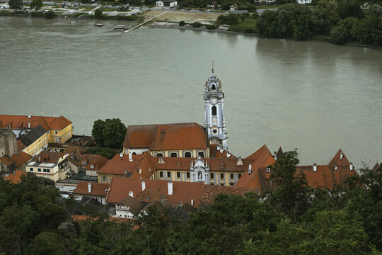 View of the iconic blue tower of Stift Durnstein Abbey along the Danube river, surrounded by historic terracotta-roofed buildings and lush greenery in Durnstein, Lower Austria, Austria.