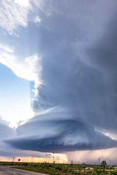 View of a massive supercell storm cloud with a rotating wall cloud and heavy rain over a flat rural landscape with power lines.