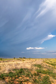 View of a dramatic dark storm cloud formation over a dry grassy field under a vast sky.