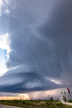 View of a dramatic supercell storm with dark swirling clouds and rain shafts over an oil pump jack in a rural field in Oklahoma City, Oklahoma, United States.