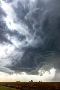 View of a massive supercell storm with dark, swirling clouds and heavy rain shafts over a flat rural landscape in Oklahoma City, Oklahoma, United States.