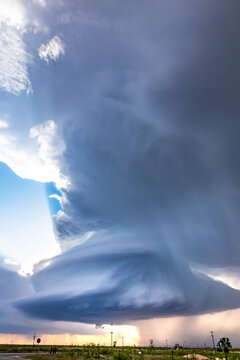 View of a massive supercell storm cloud with dark swirling formations and rain shafts over a flat landscape.
