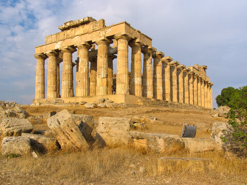 View of the ancient Greek Temple E at Selinunte Archaeological Park with weathered Doric columns and scattered stone ruins in the dry landscape of Marinella, Sicilia, Italy.