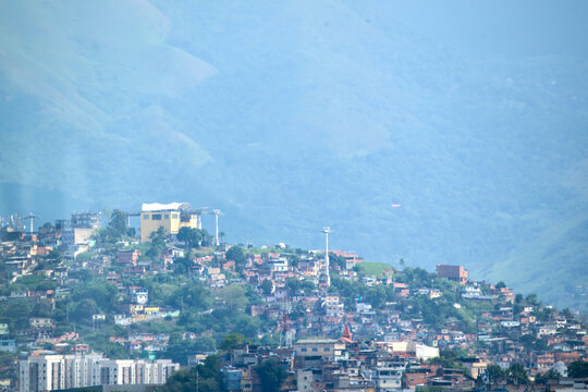 View of the Complexo do Alemao favela with its cable car station, dense hillside housing, and mountains in the background, Rio de Janeiro, Rio de Janeiro, Brazil.