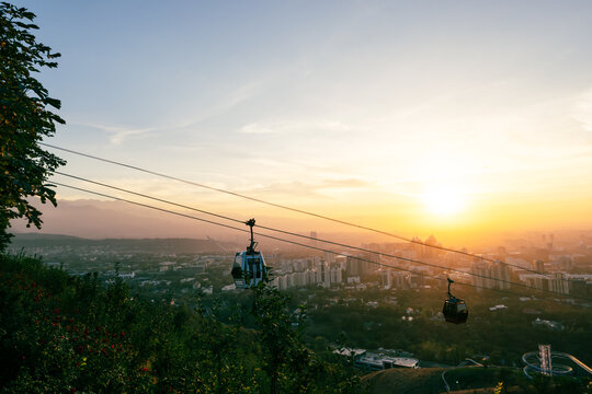 View of the Kok Tobe cable car system transporting passengers over the city of Almaty at sunset, with the Trans-Ili Alatau mountains in the background, Almaty, Almaty Region, Kazakhstan.