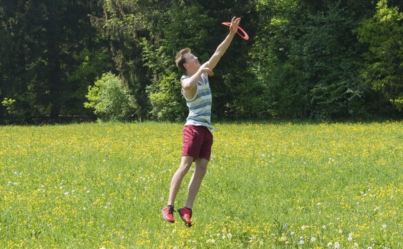 Young man catching frisbee in meadow, Perlacher Forst, Munich, Bavaria, Germany
