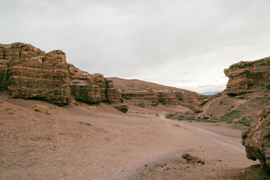 View of Charyn Canyon National Park featuring layered sedimentary rock formations and a winding dirt path under an overcast sky in Tamerlik, Almati oblisi, Kazakhstan.