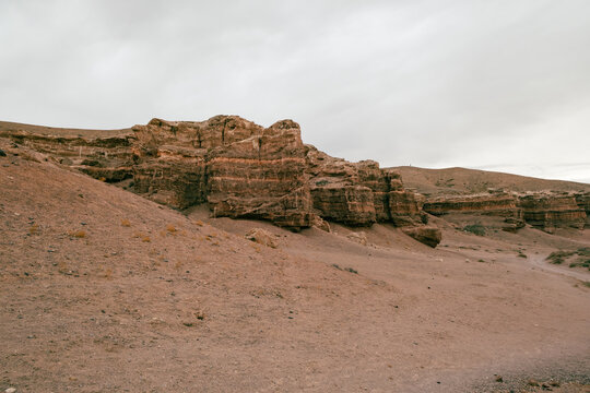 View of the rugged rock formations and layered sedimentary cliffs of Charyn Canyon National Park under an overcast sky in Tamerlik, Almaty, Kazakhstan.