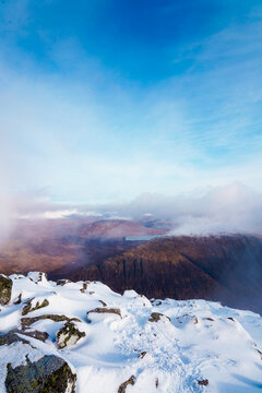 View of snow-covered mountain peak with rocky outcrops and low-hanging clouds over the valley in Glencoe, Scotland, United Kingdom.