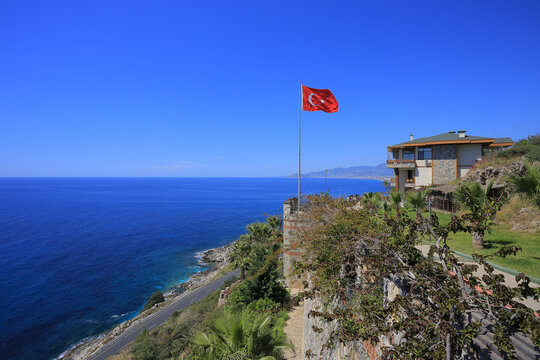 Red flag of Turkey on a high pole near a luxury seaside villa under a blue sky