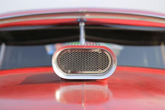 Close up of a custom chrome air scoop on a red car hood
