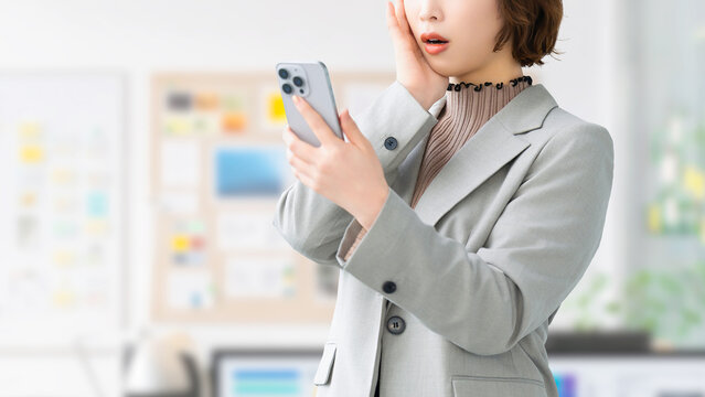 スマートフォンを見て驚く女性・ビジネスウーマン