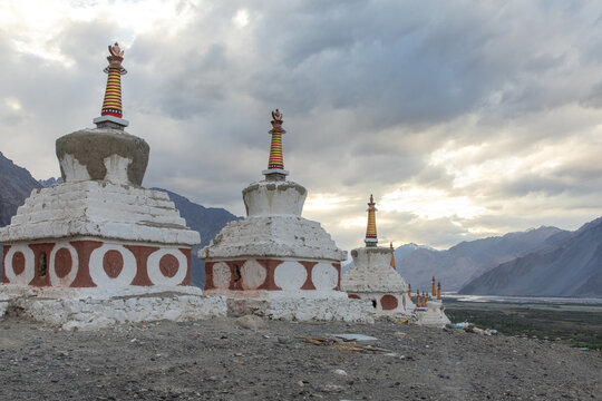 View of the historic Buddhist stupas in Nubra Valley with golden spires and red circular patterns set against a dramatic mountain landscape in Diskit, Ladakh, India.