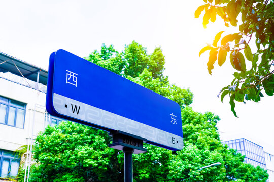 Street direction sign with East E West W Chinese characters, sunny urban street in China