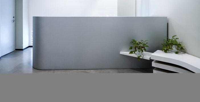 Minimalist grey curved reception desk with white layered bench and green pothos plants in modern office lobby