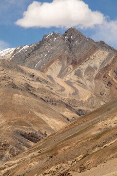 View of the rugged, stratified mountain peaks of the Zanskar range with visible geological rock formations, patches of snow, and a clear blue sky in Zanskar, Ladakh, India.
