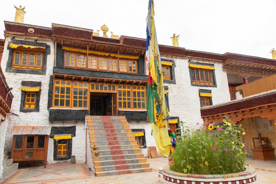 View of the traditional architecture of a Buddhist monastery in Zanskar with white walls, ornate wooden windows, a central stone staircase, and a tall prayer flag. Zanskar, Ladakh, India.
