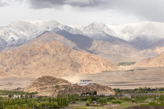 View of Leh Palace perched on a rocky hill overlooking the green valley with snow-capped Himalayan mountains in the background in Leh, Ladakh, India.