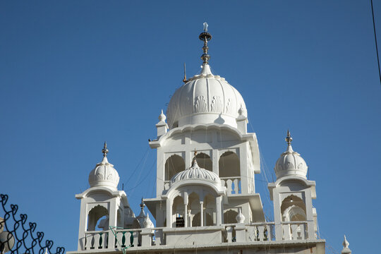 View of the white domes and intricate arched architecture of a Sikh temple against a clear blue sky in Leh, Ladakh, India.