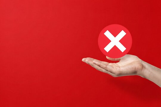 Hand holding a red circle with white cross mark symbol isolated on a solid red background surface