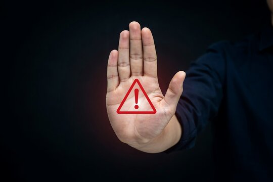 Human hand showing stop gesture with red warning triangle symbol isolated on dark black background surface