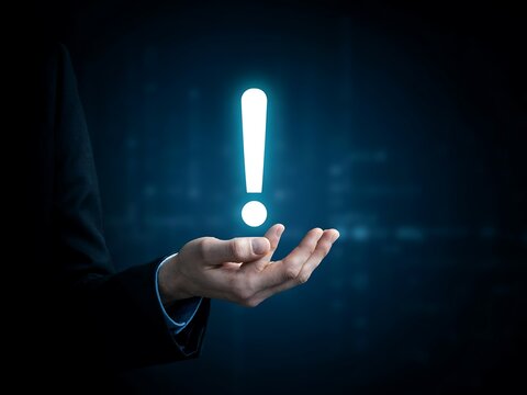 Glowing white exclamation mark floating above an open palm of a businessman in a dark blue background