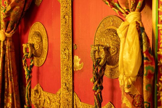 View of the ornate red doors with intricate gold metalwork and dragon-shaped door knockers at Namobuddha Monastery in Simalchaur Syampati, Bagmati Province, Nepal.