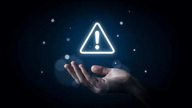 Glowing white warning triangle icon floating above open human palm against dark blue digital background space