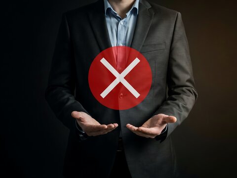 Businessman holding red circle with white cross symbol representing rejection or error in professional corporate setting
