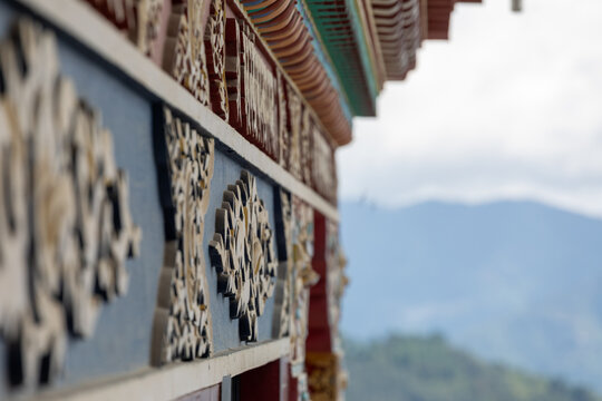 View of intricate and colorful traditional architectural carvings on the exterior of Namobuddha Monastery, with blurred mountains in Simalchaur Syampati, Bagmati Province, Nepal.